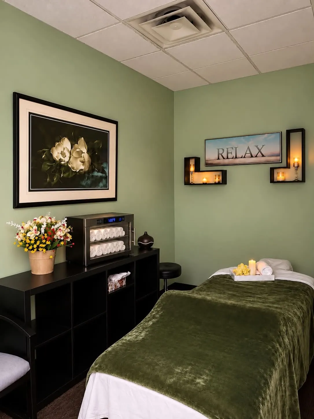 Green massage room with a prepared table, fresh towels, and a towel warmer